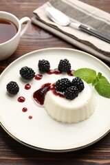 Tasty panna cotta with blackberries, mint and sauce on wooden table, closeup