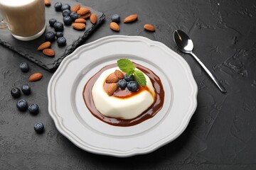 Tasty panna cotta with blueberries, almonds and sauce on black table, closeup
