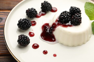 Tasty panna cotta with blackberries, mint and sauce on wooden table, closeup