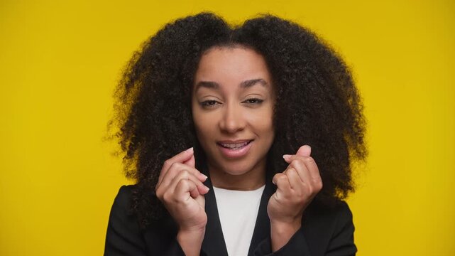 Smirking woman making money gesture on yellow background