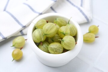 Fresh green gooseberries in bowl on white table, closeup