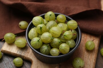 Fresh green gooseberries in bowl on wooden table, closeup