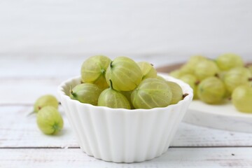 Fresh green gooseberries in bowl on white wooden table, closeup