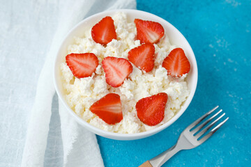 bowl of cottage cheese with strawberries and fork on blue background