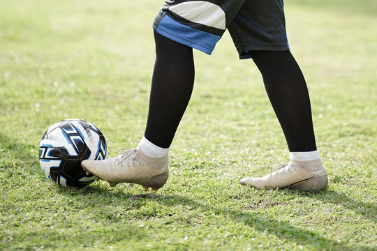 Close-up shot of a football player's foot on a modern soccer ball. Athlete in cleats and socks on a green training pitch.