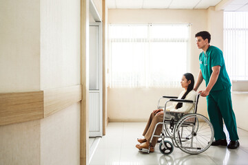 Male nurse in green scrubs assists female patient in a wheelchair along a bright hospital corridor, representing patient care, accessibility, and modern healthcare support in a clinical setting.
