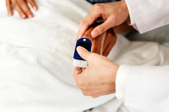 Close-up of a doctor’s hand using a pulse oximeter on a patient’s finger in a hospital bed, representing medical monitoring, healthcare technology, patient care, and hospital diagnostic support. - Powered by Adobe