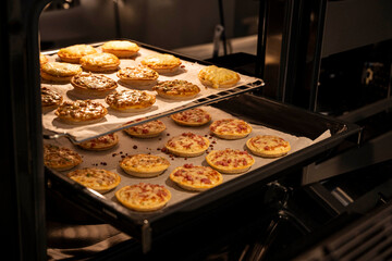 A tray of pizza and a tray of pastries are in an oven. The oven is open and the pastries are on the...