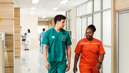 Diverse medical professionals in scrubs walk through a bright hospital hallway, engaged in conversation. Represents teamwork, inclusive healthcare workforce, and professional hospital care.