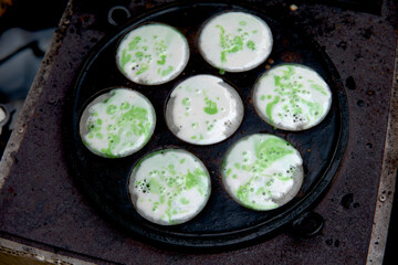Traditional kue bikang baking: vibrant green and white batter cooks in a multi-mold pan. This soft, sweet cake, often with coconut milk, is a delicious classic.