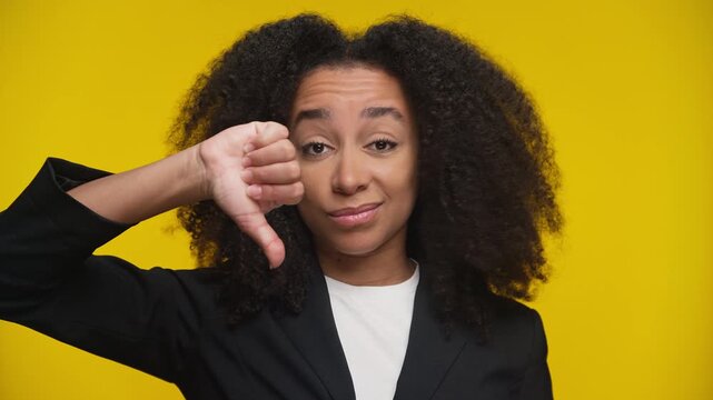 Displeased woman showing thumbs down on yellow background