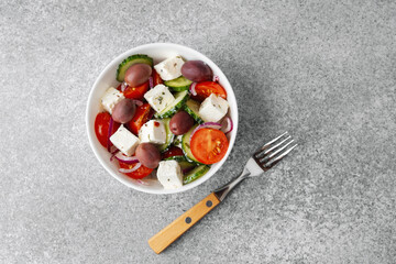 Greek salad with feta cheese olives cucumbers tomatoes onions in white bowl with fork on light grey...