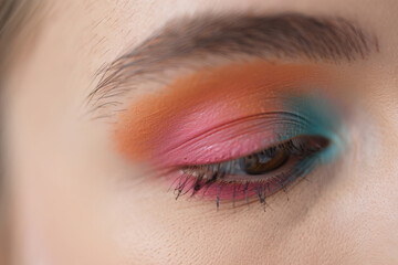 Obraz premium Closeup of a womans eye with vibrant pink, orange, and teal eyeshadow, showcasing a bold and artistic makeup look