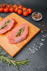 Top view of veal steaks with rosemary on wooden cutting board and cooking ingredients