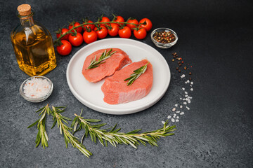 Raw veal steaks on white ceramic plate with tomatoes herbs salt oil and pepper