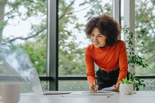 Businesswoman working at laptop in modern office with window view
