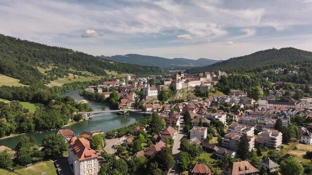 Aarburg town and river Aare aerial view, castle on rocky hill, meandering river, forested hills and Swiss architecture under cloudy sky.