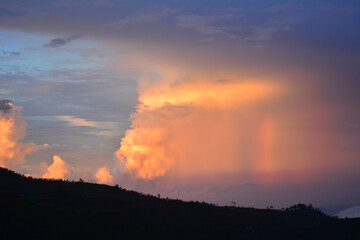 Fototapeta premium A dramatic sunset sky over a dark landscape, featuring a large, illuminated cloud formation and a subtle rainbow or light beam. Related to atmospheric phenomena, dramatic skies, tranquility of dusk