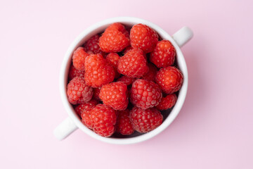 Top view of raspberries in cup on pink background for diet blog or fruit branding concept