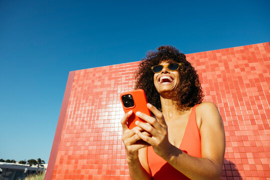 Happy woman laughing while using her mobile phone on a summer day at the beach
