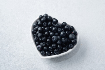Blueberries in heart-shaped bowl on white for health, love or superfood concept
