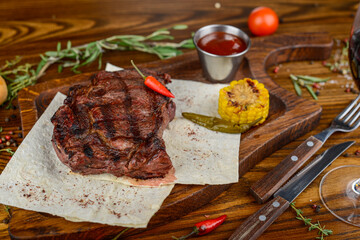 huge grilled steak on parchment on a wooden board with corn and sauce