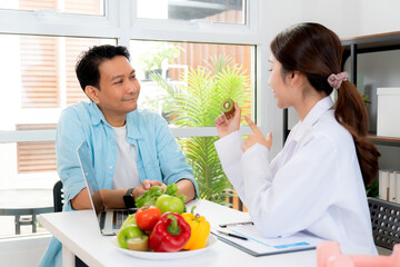 Asian nutritionist holding fresh fruits vegetables during consultation with patient in clinic, wellness and healthy eating, woman dietitian or consultation explaining nutrition for weight loss advice.