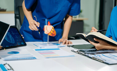 Group of medical students in uniform studying heart anatomy with tablet, notes, and lab reports in...