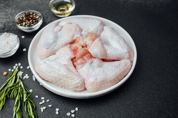 Raw chicken wings with spices herbs and oil on dark stone background
