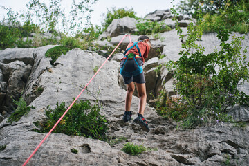 Obraz premium Boy climbing high natural rock wall with rope in mountain setting
