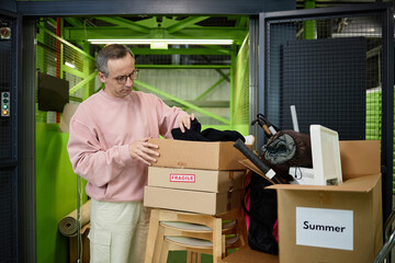 Middle aged Caucasian man packing cardboard boxes labeled fragile and summer in storage facility,...