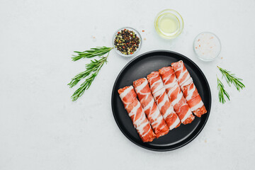 Bacon wrapped sausages on black plate with spices and rosemary