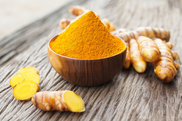 Turmeric powder and fresh turemric in wood bowls on old wooden table. Herbs are native to Southeast Asia.