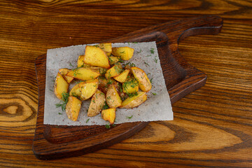 fried grilled potatoes in slices on parchment on a wooden board on a wooden background