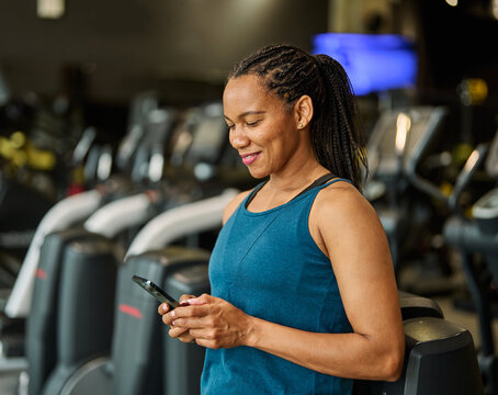 Portrait of a young black woman using a phone ant exting taking a break exercising in a gym, running using  thereadmill machine equipment, healthy lifestyle and cardio exercise at fitness club concept