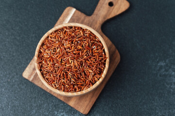 Red rice in wooden bowl placed on cutting board over dark surface