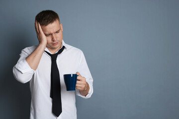 Man with cup of drink suffering from hangover on grey background, space for text