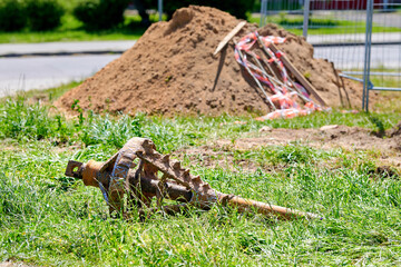 Closeup of used auger drill bit lying on green grass at an outdoor construction site with soil pile in the background under sunny weather.  Spiral auger head left near construction pit. Hdd drill work