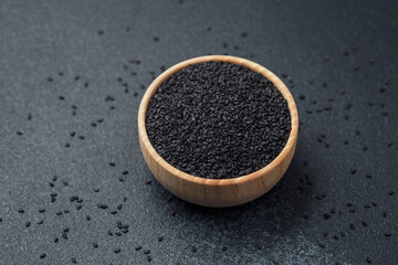 Black sesame seeds in bowl on dark background