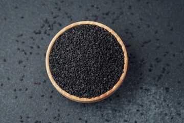 Black sesame seeds in bowl on dark background