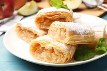 Pieces of tasty apple strudel with powdered sugar and mint on light blue wooden table, closeup