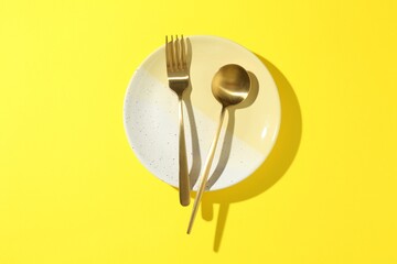 Stylish plate and cutlery on yellow background, top view