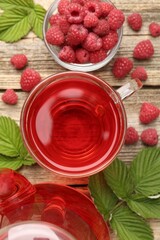 Tasty raspberry tea, berries and leaves on wooden table, flat lay