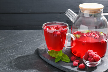 Aromatic raspberry tea in glass cup, teapot, berries and mint on black table, closeup. Space for text