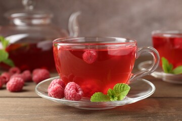 Tasty raspberry tea in glass cups, teapot, berries and mint on wooden table, closeup