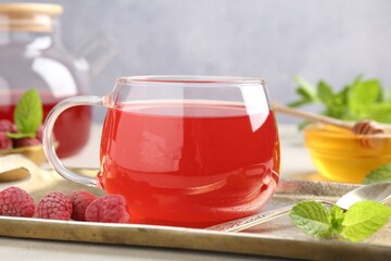 Tasty raspberry tea, berries, honey and mint on light grey table, closeup
