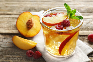 Iced tea. Refreshing drink with peach and raspberries in glass on wooden table, closeup