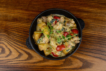 Potato fries with tomatoes and cheese in a frying pan on a wooden background