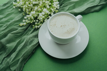 Cup of coffee with milk and lily of the valley flowers on green textile background