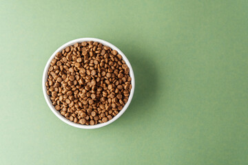 Top view of dry dog food in white bowl on green background